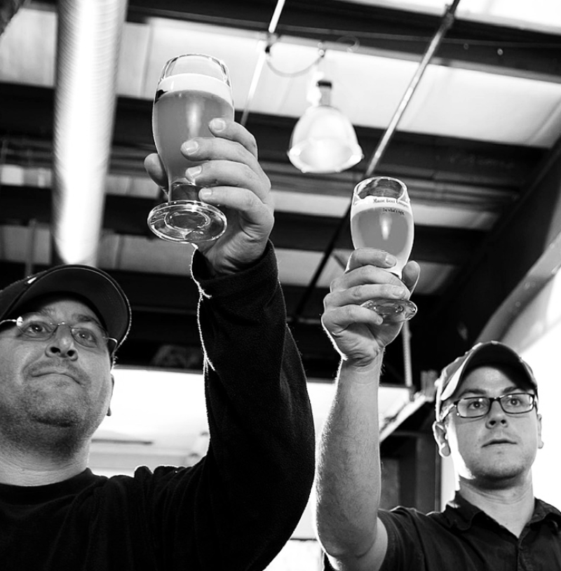 A black and white photo of co-founders and brothers David and Daniel Kleban raise glasses of their beer.