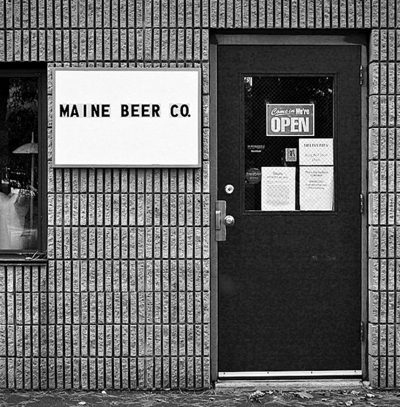 A black and white photo of Maine Beer Company's original location in Portland, with a simple white sign.