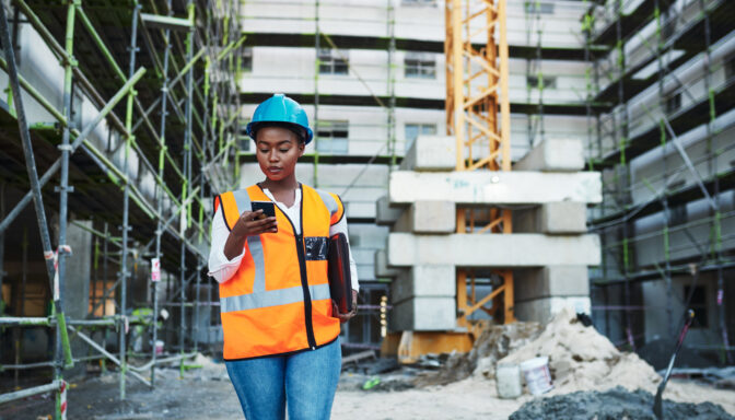 Project manager in a construction setting looking at her phone reading a work related text message.