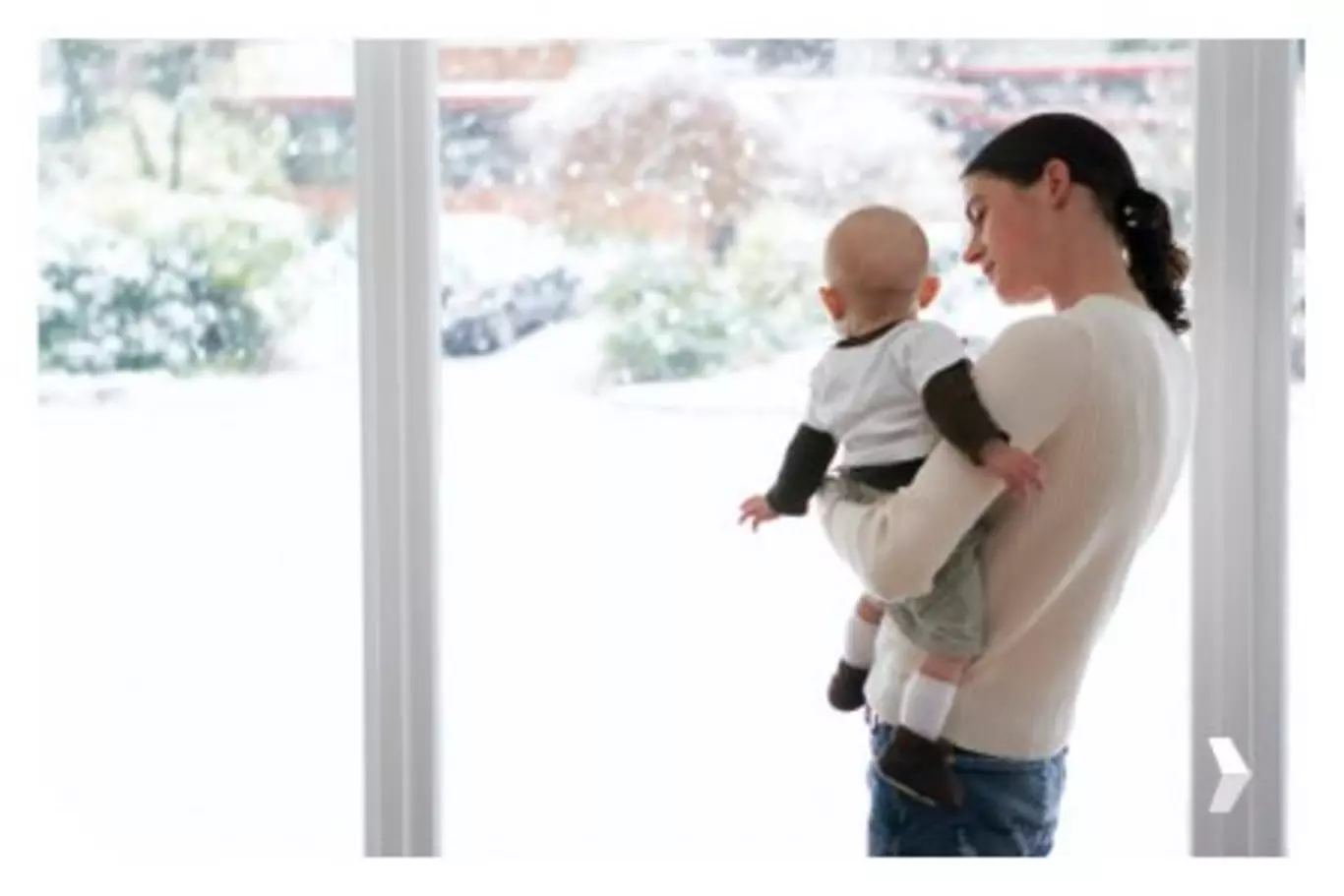 Mother and baby boy looking out window at snow.
