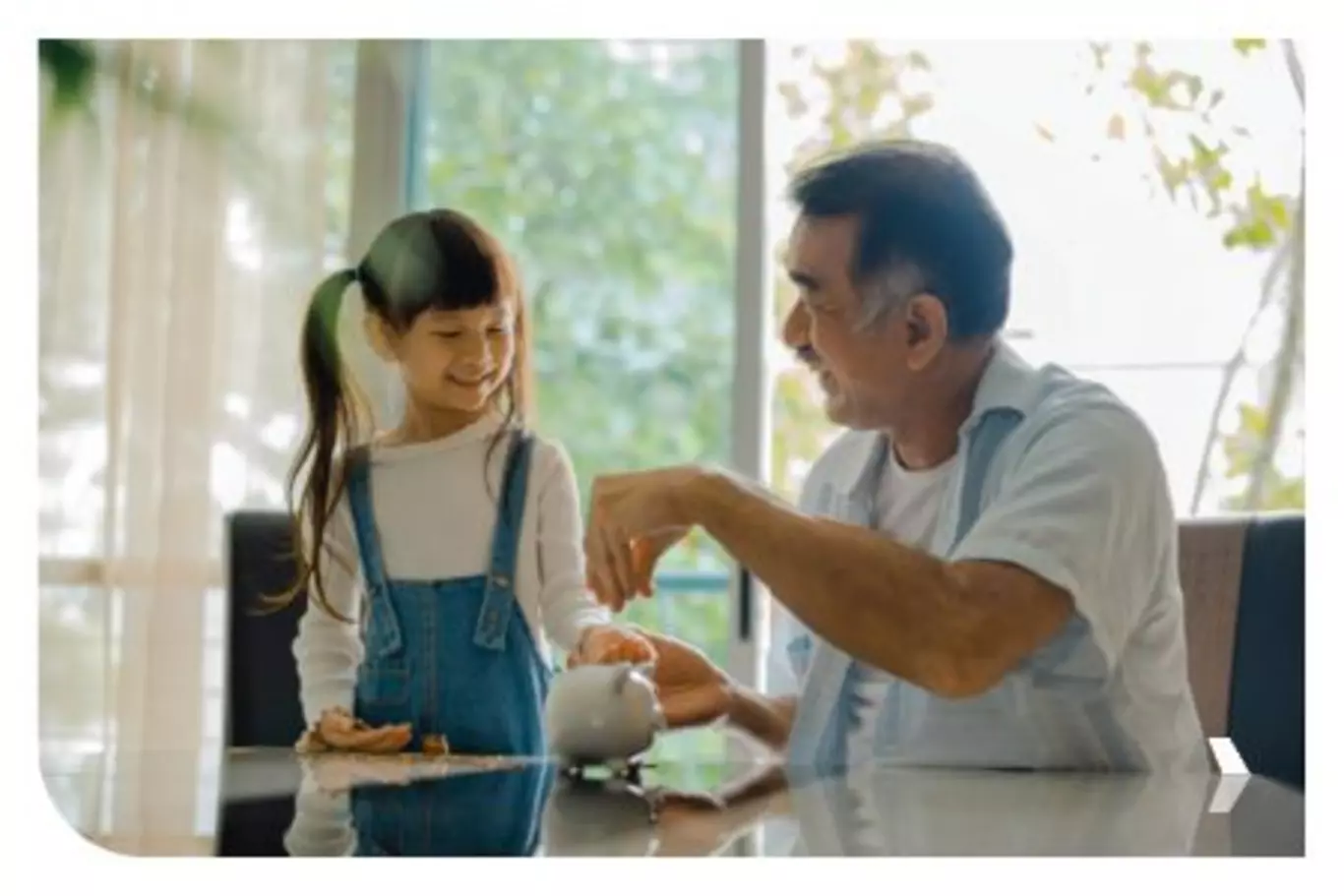 Little girl putting coins into piggy bank with her grandfather