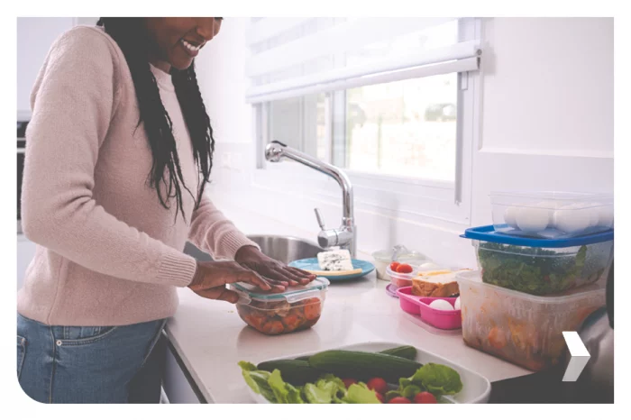 Young woman packing leftovers into plastic container in the kitchen